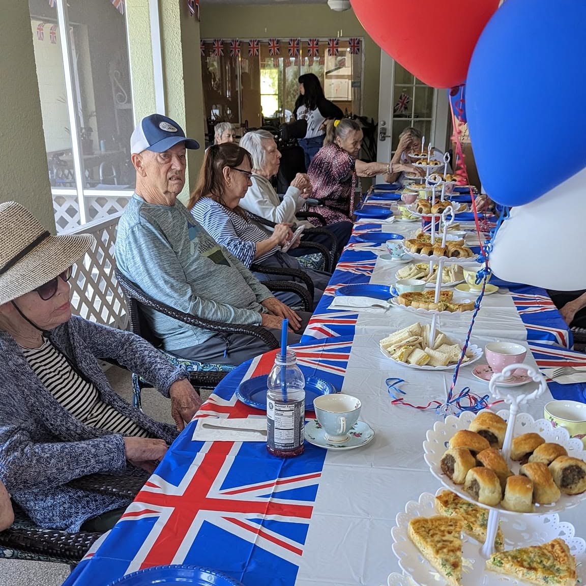 Long-table British-themed tea party with residents on the covered porch